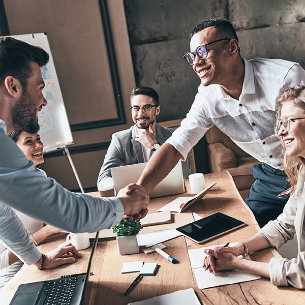 Welcome to our team! Top view of young modern men in smart casual wear shaking hands while working in the creative office